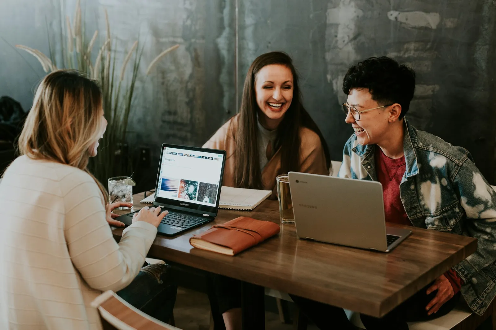 Três pessoas conversando e rindo em uma mesa de trabalho
